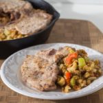 A skillet with pork chops and vegetables on it.