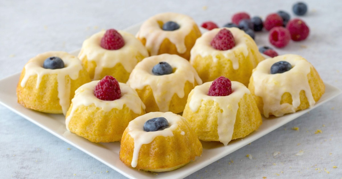 Mini lemon bundt cakes on a cool rack drizzled with icing and topped with raspberries and blueberries.