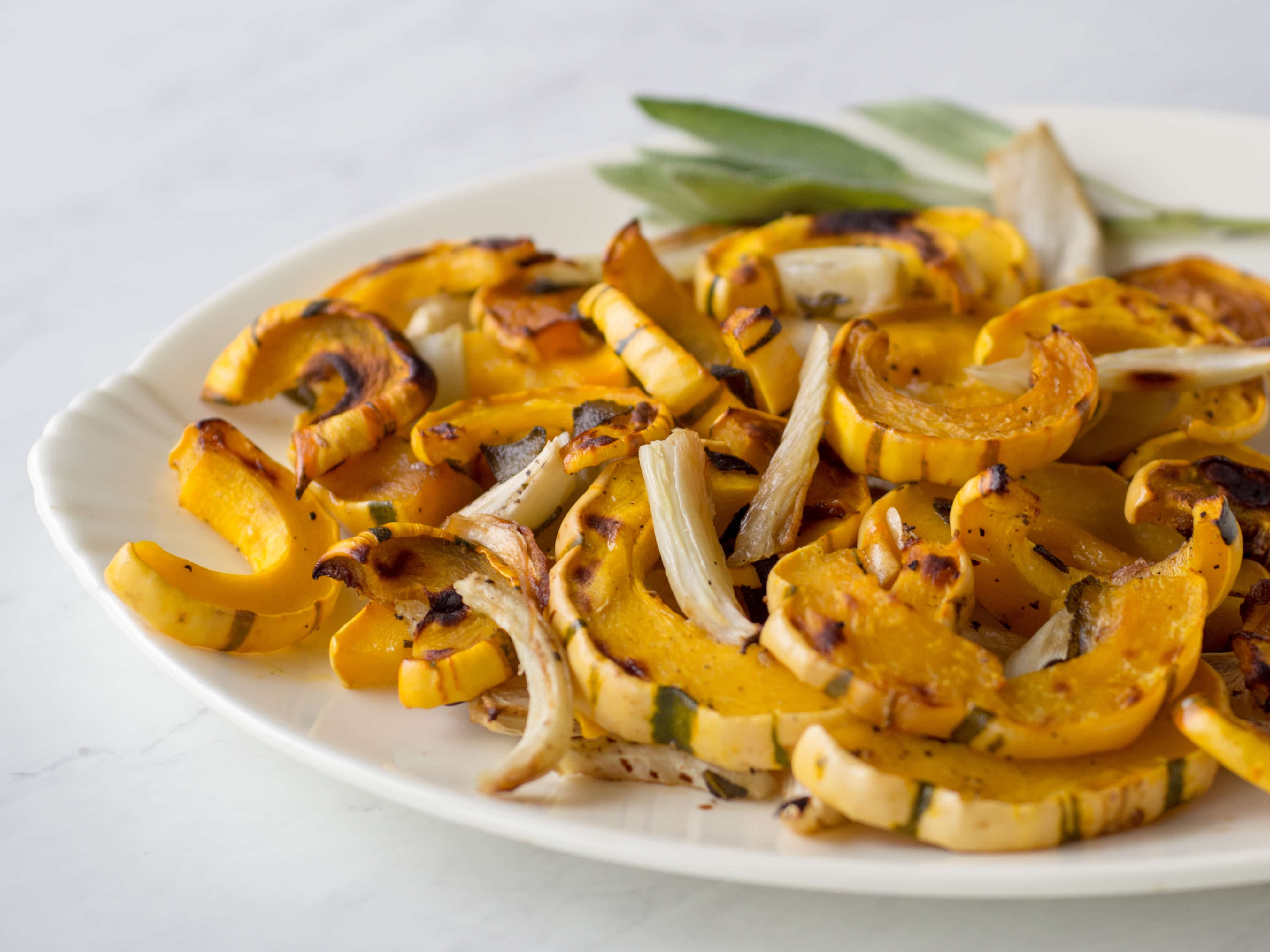 Roasted delicata squash with sage leaves on a white plate.