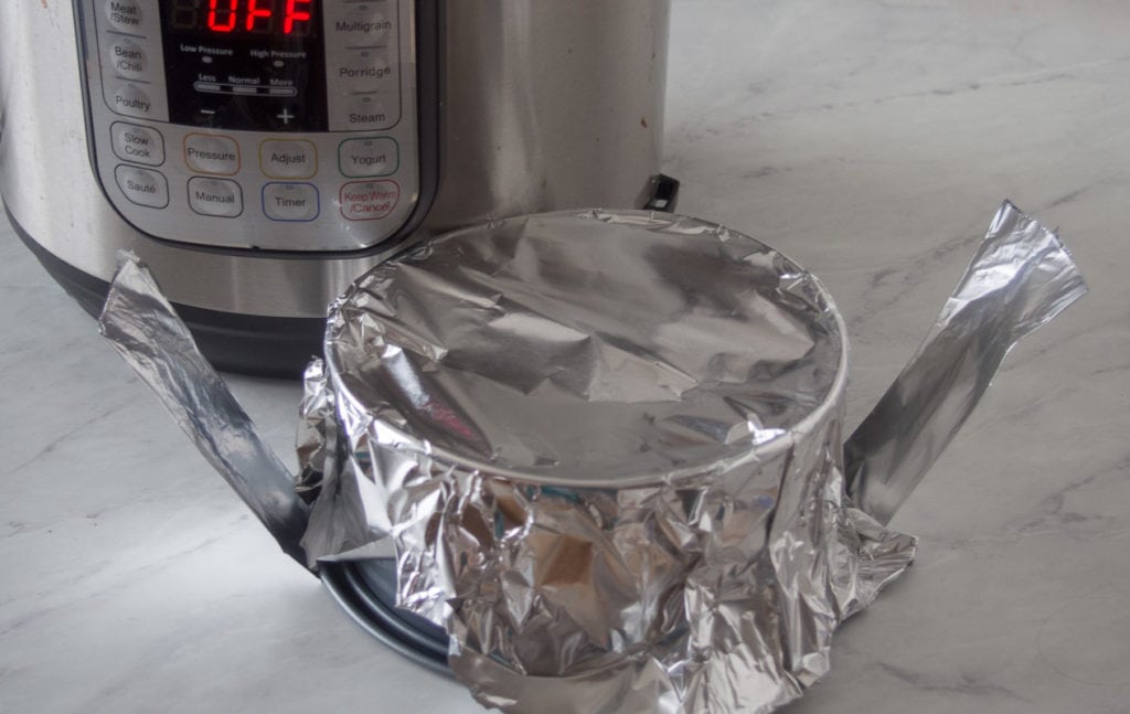 cheesecake covered in foil next to pressure cooker