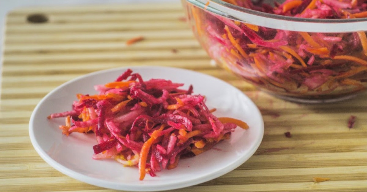 Grated beets, apples and carrots on a spoon.