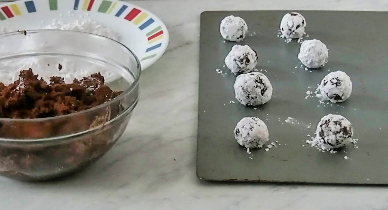 rolling the chocolate crackle cookies in powdered sugar