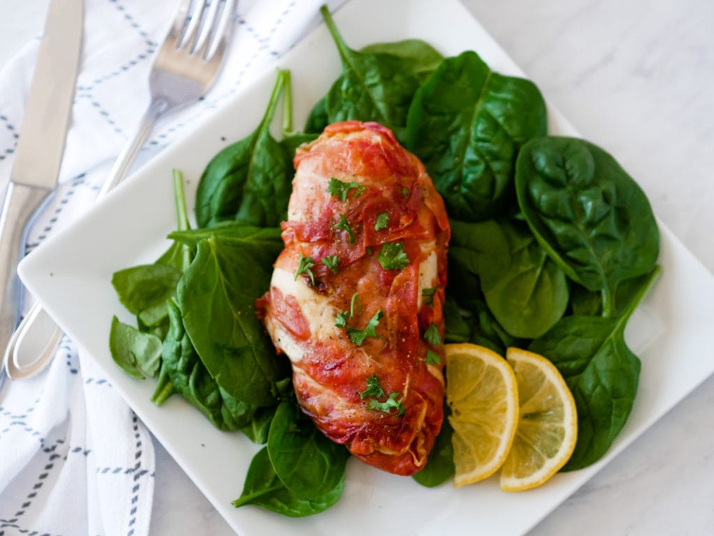 top view of chicken wrapped in prosciutto on a plate on a bed of spinach
