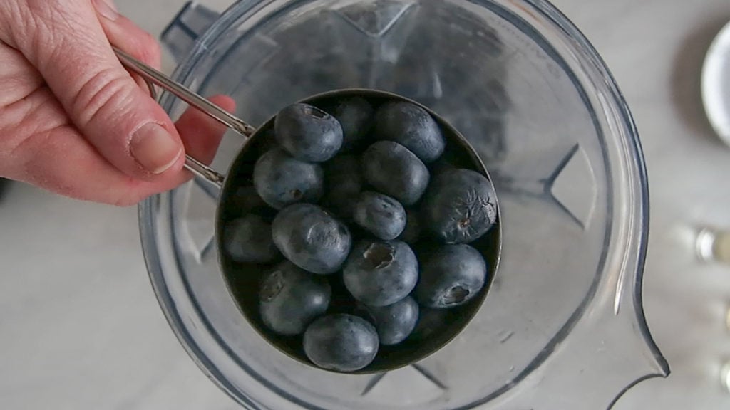 adding blueberries to the blender for a blueberry margarita