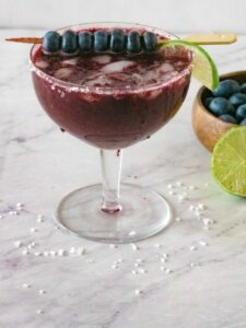 blueberry margarita in a glass garnished with lime and blueberries