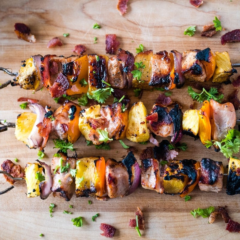 Three pork kabobs with pineapple on a wooden cutting board.
