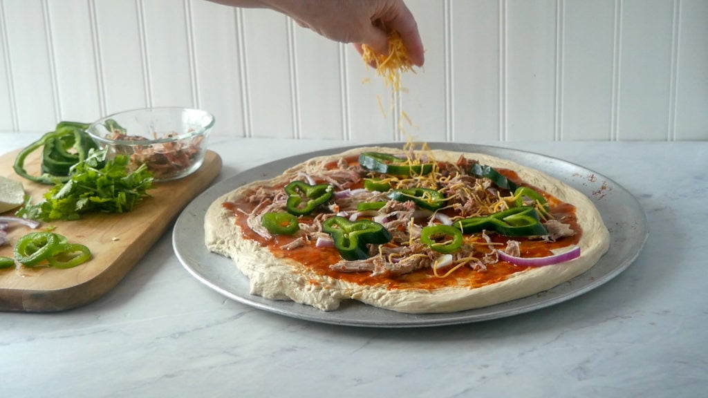sprinkling cheese over the pulled pork pizza