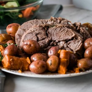 sliced instant pot leg of lamb on a plate with potatoes and carrots