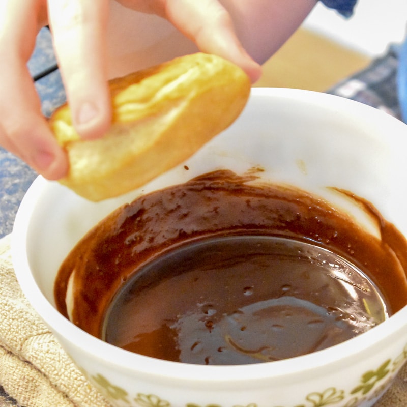 dipping a donut in a bowl of chocolate glaze