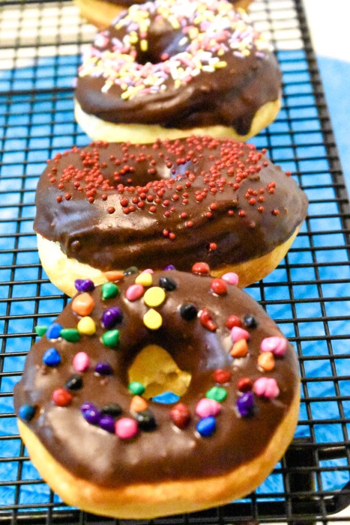 baking rack with lots of air fryer donuts glazed in chocolate and decorated with sprinkles and chips