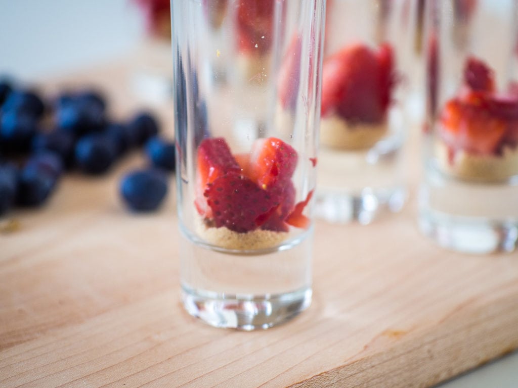 Adding strawberries to a shot glass for a no bake cheesecake