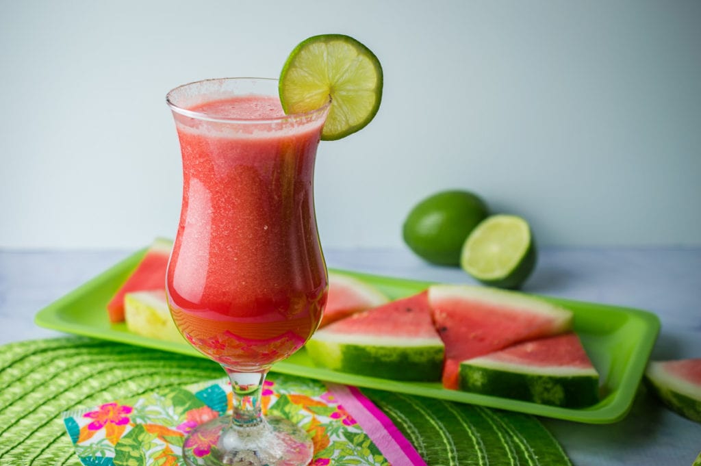 watermelon cocktail with watermelon and lime on a tray in background
