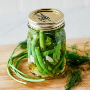 jar of dilly beans on a cutting board with dill