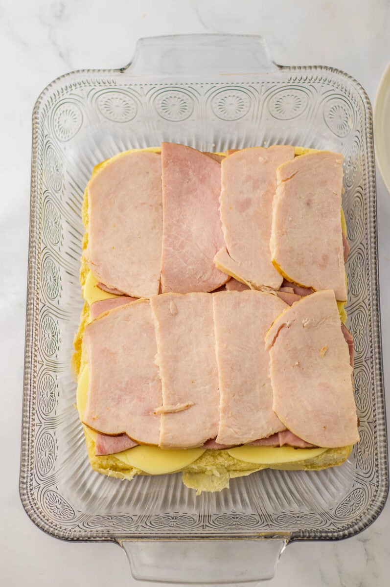 Sliced turkey sliders with cheese in a glass baking dish.