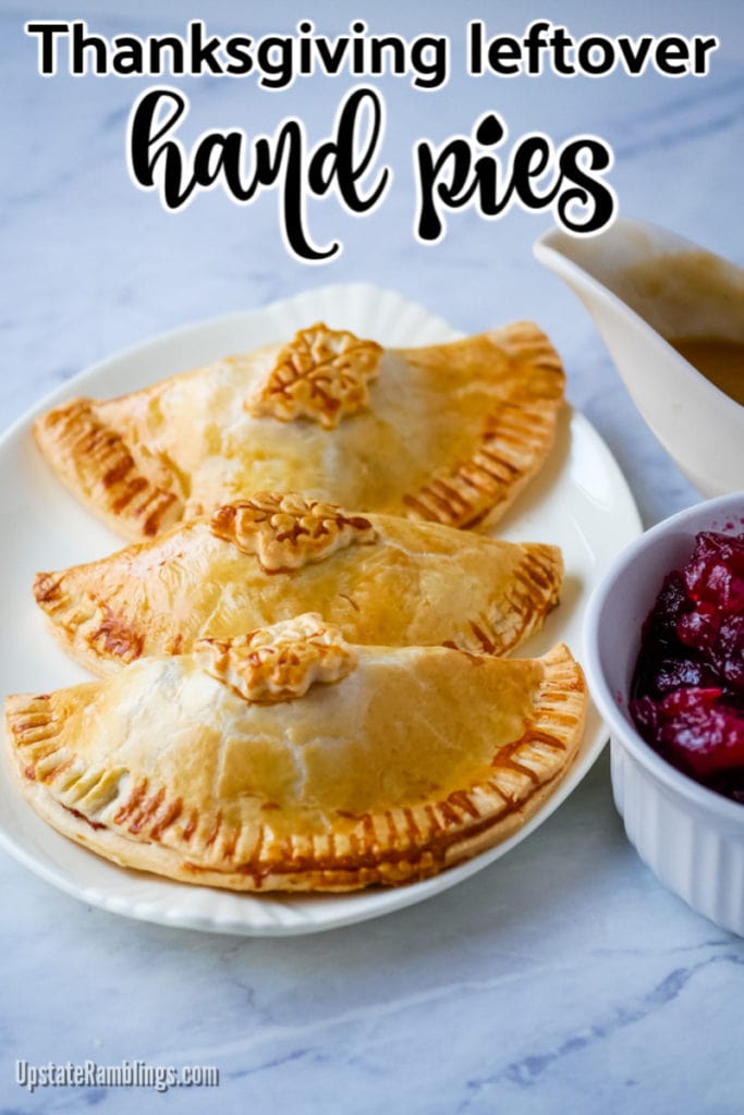 three thanksgiving leftover hand pies on a plate next to gravy and cranberry sauce