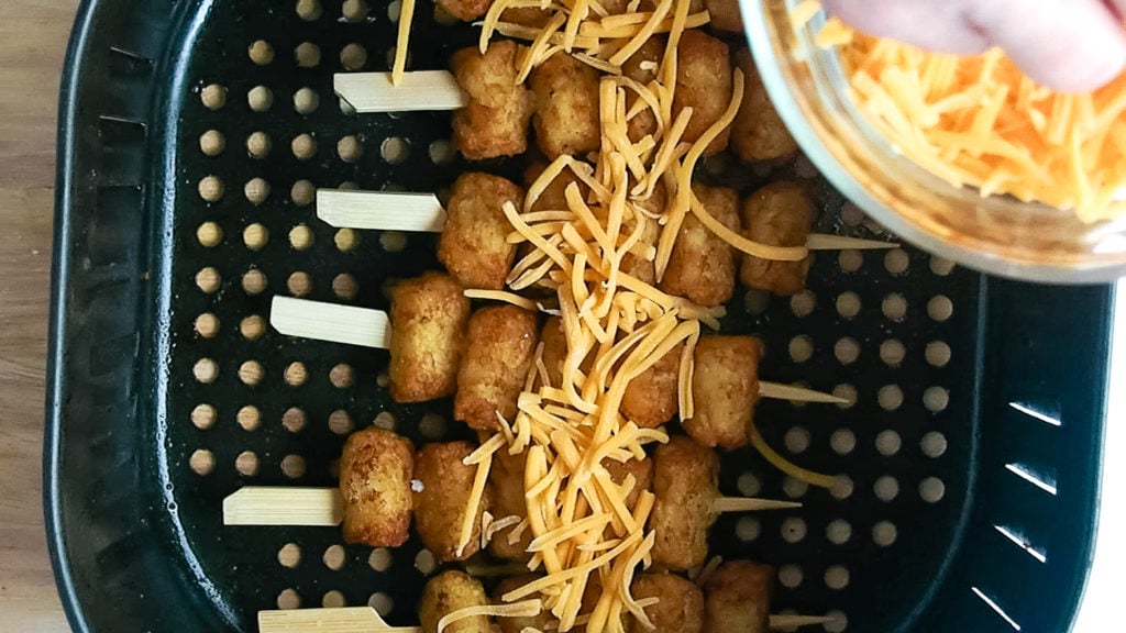 adding cheese to the tater tot skewers