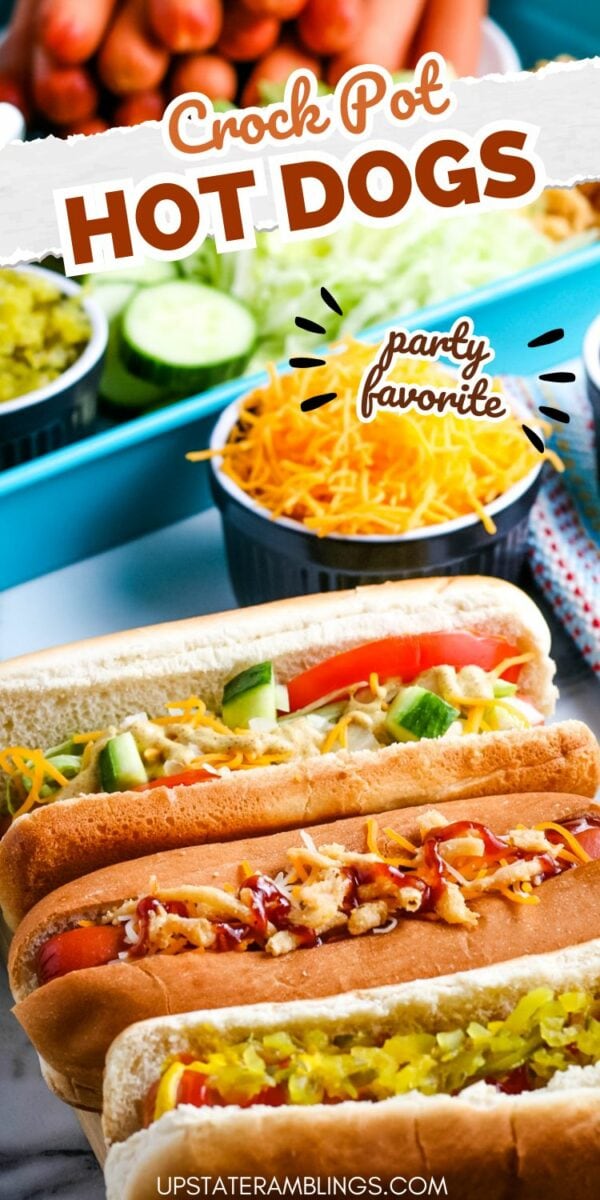 Four crock pot hot dogs with various toppings such as relish, cheese, onions, and tomatoes are lined up on a tray. Bowls of shredded cheese and sliced cucumbers are in the background.
