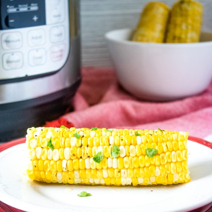 ear of corn on a plate with more corn and pressure cooker in background