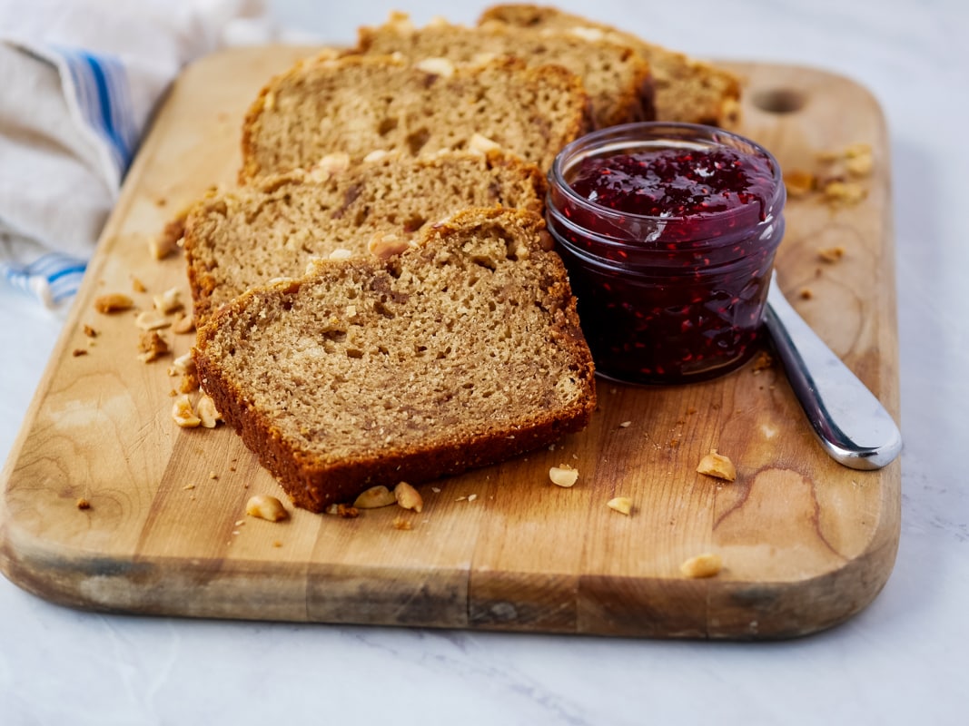 Slice peanut butter bread on a cutting board with a jar of raspberry jam and knife.