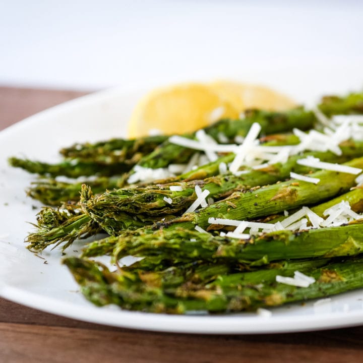 asparagus on a plate topped with cheese with lemon in the background