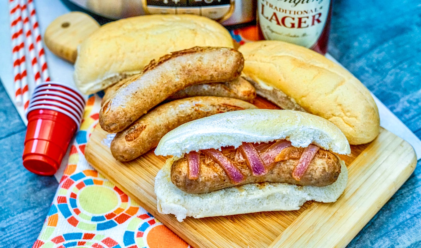 Brats and beer served on a cutting board.