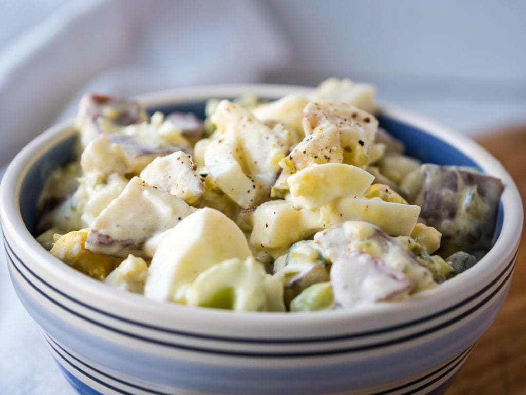 close up of a bowl of potato salad with eggs, celery and gherkins
