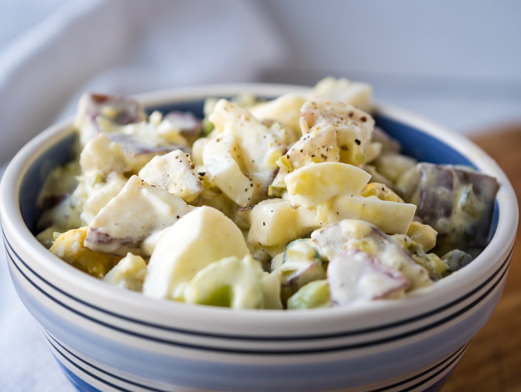Potato and egg salad in a blue striped bowl.