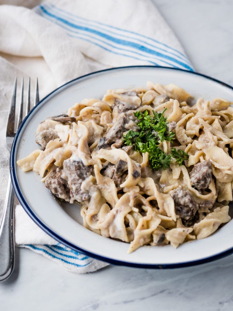 plate of beef stroganoff topped with parsley next to a fork and a dish towel