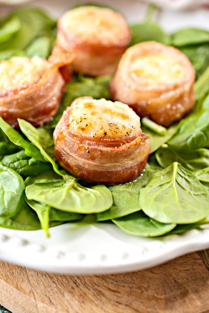 bacon wrapped scallops on spinach on a white plate