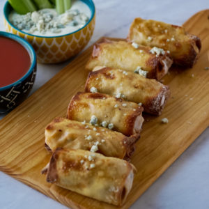 Buffalo egg rolls on a wooden cutting board with bowls of dip in the background
