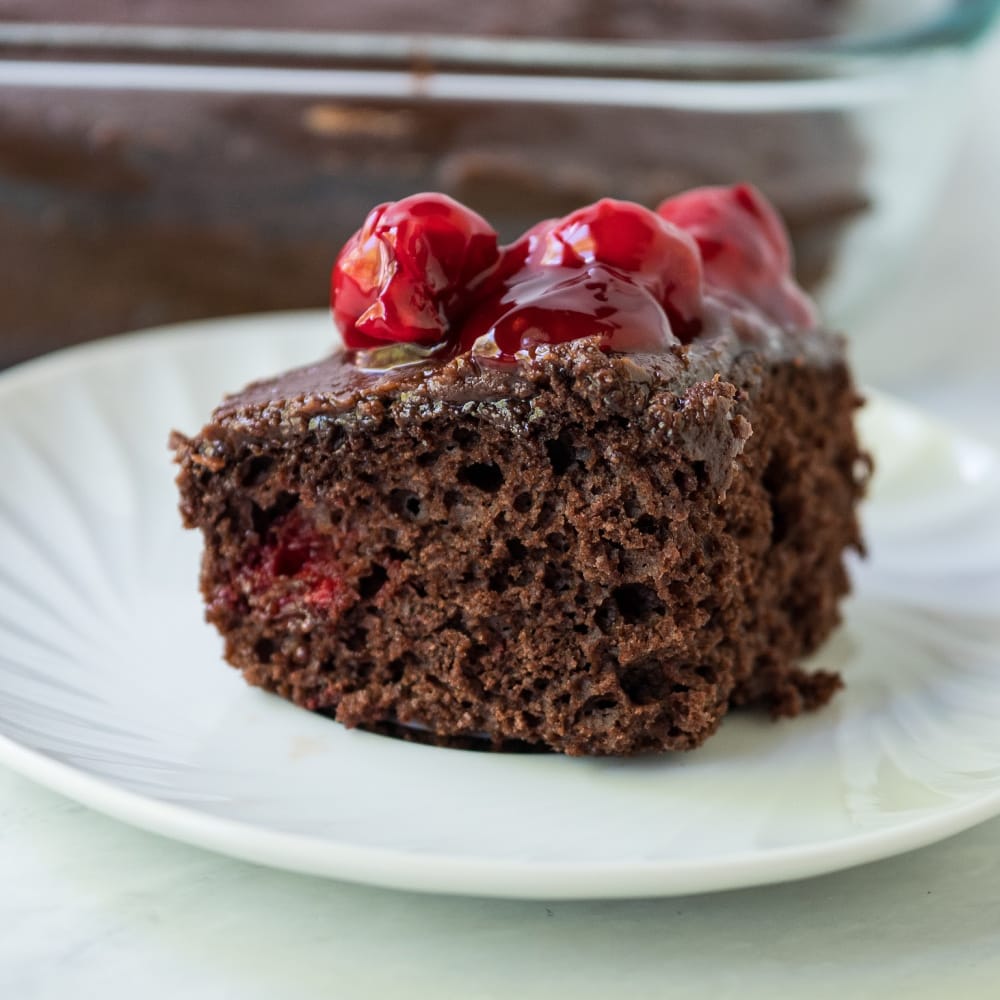 slice of chocolate cherry cake on a plate with cherries on top