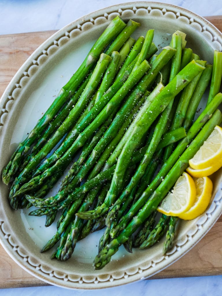 top view of asparagus stalks on a platter with lemon wedges