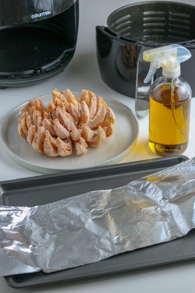 An air fryer is on a tray next to a bottle of oil and a blooming onion.