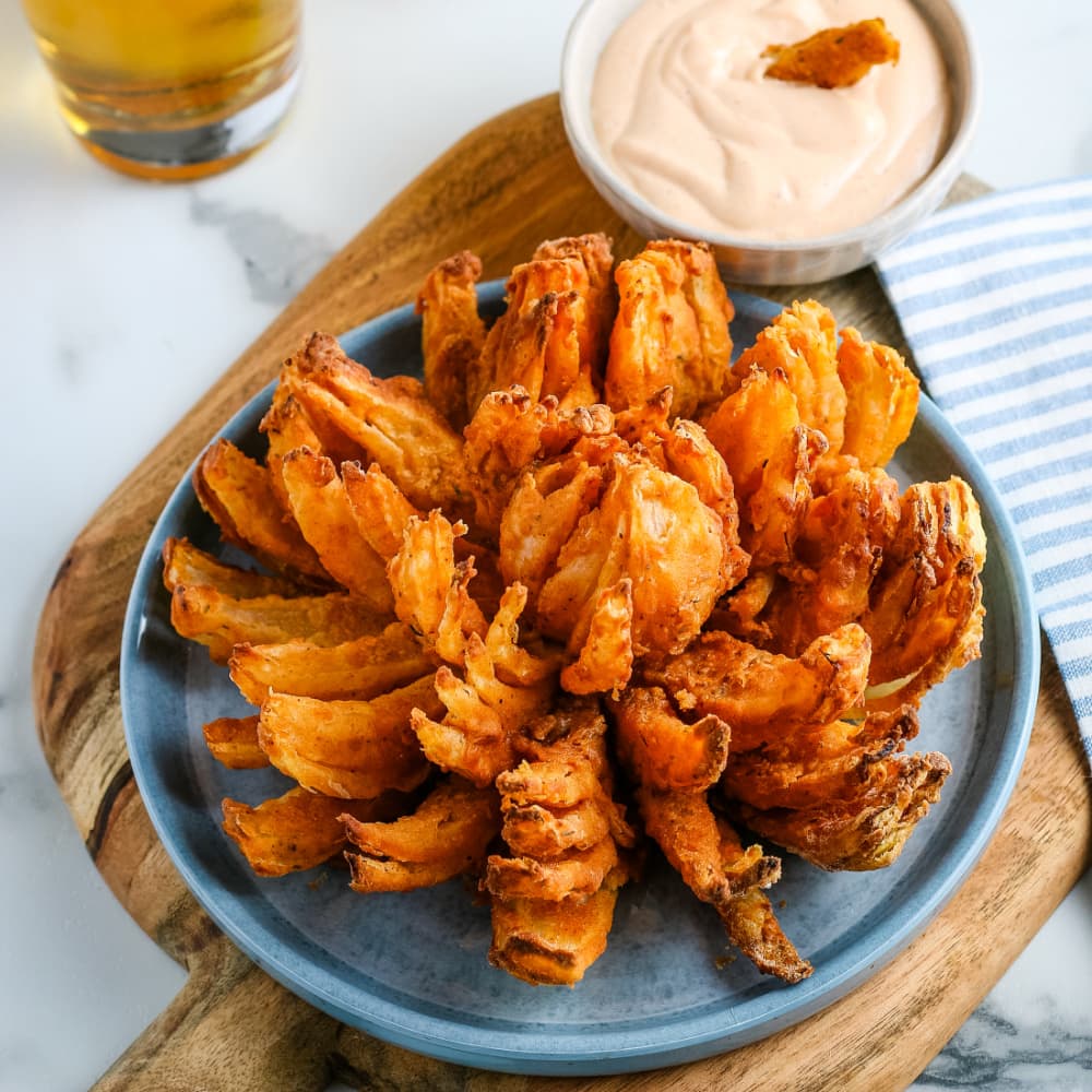 Air-fryer blooming onion on a plate with dipping sauce.