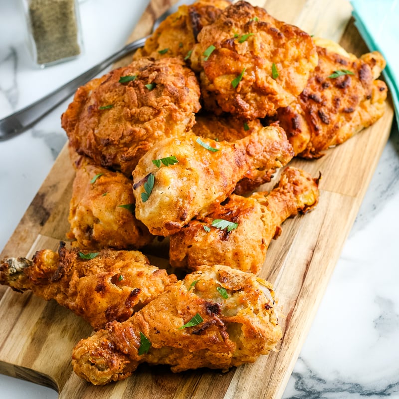 Air fryer fried chicken legs and thighs in a pile on a wooden cutting board.
