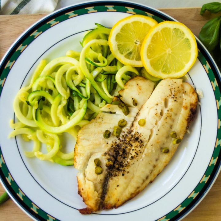 top view of tilapia on a plate with basil and garlic scapes
