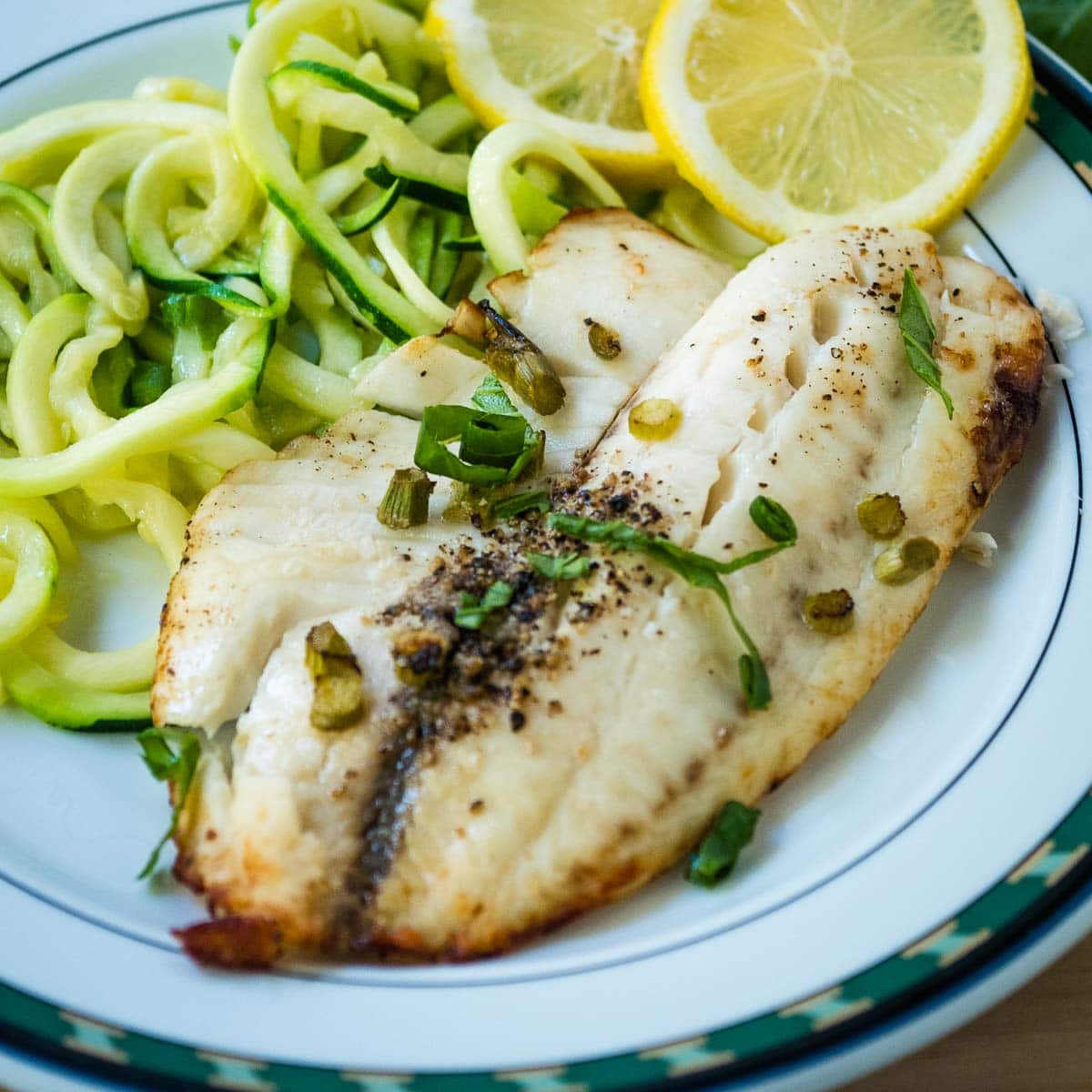Air fryer tilapia fillet on a plate with zucchini and lemon.