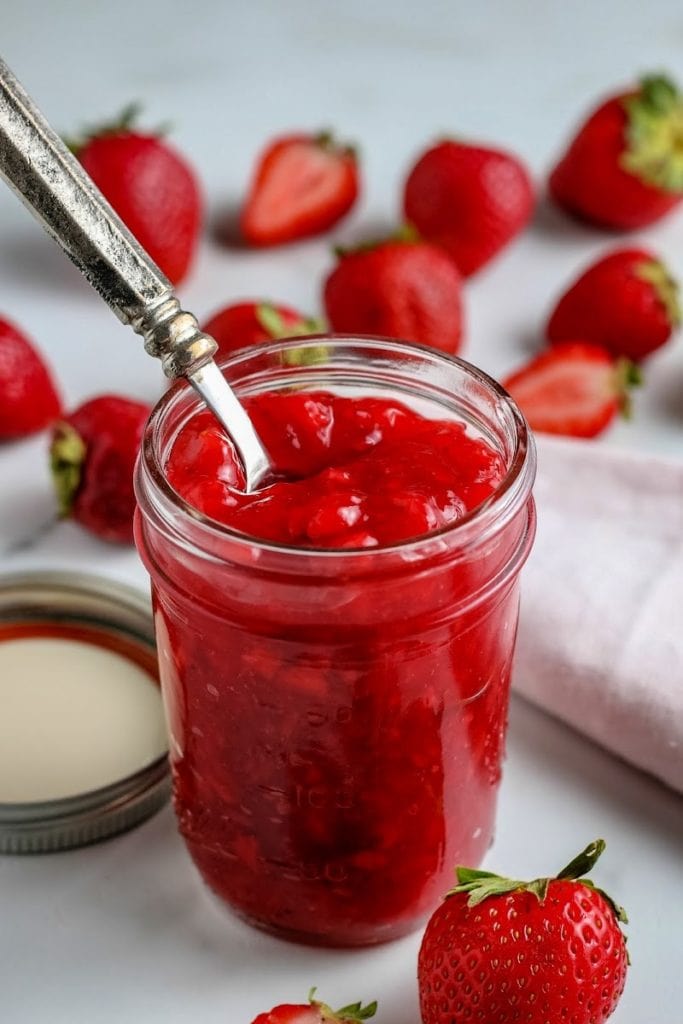 mason jar full of strawberry sauce with berries in the background