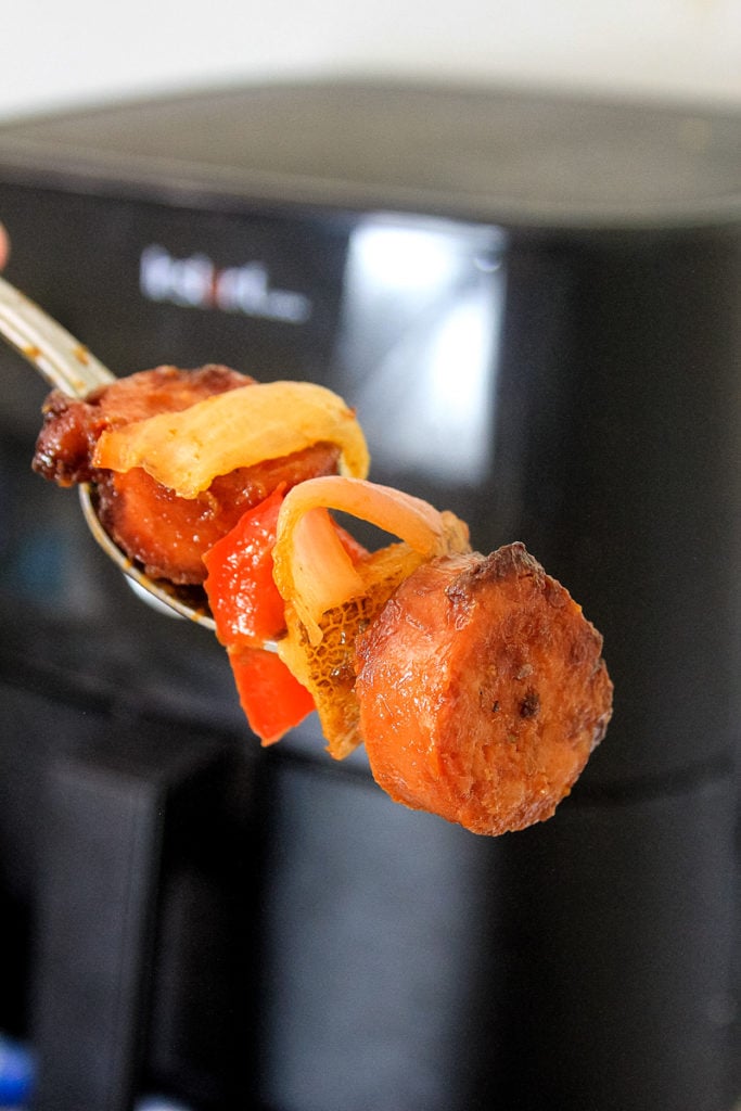 forkfull of kielbasa and vegetables in front of an air fryer