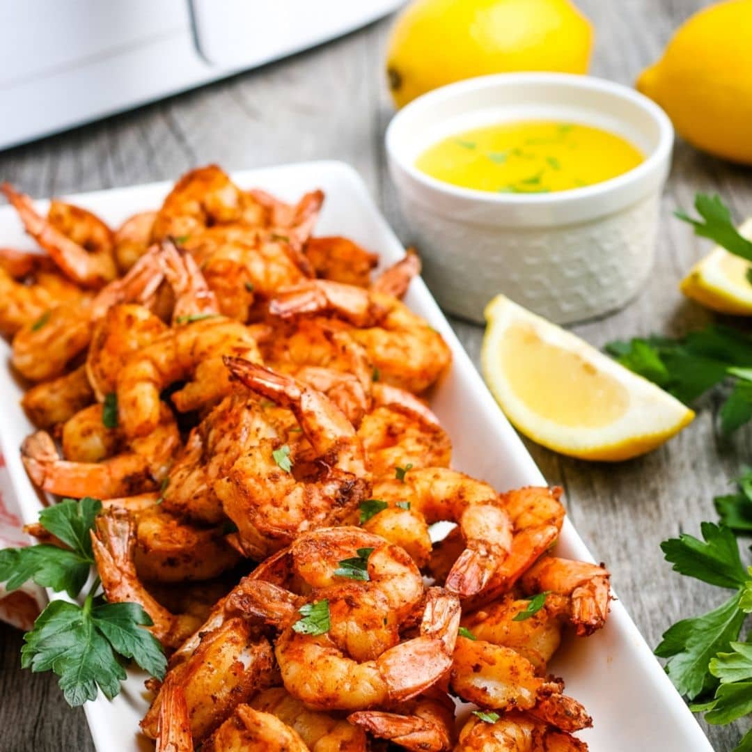 Platter of shrimp after air frying with drawn butter in the background.