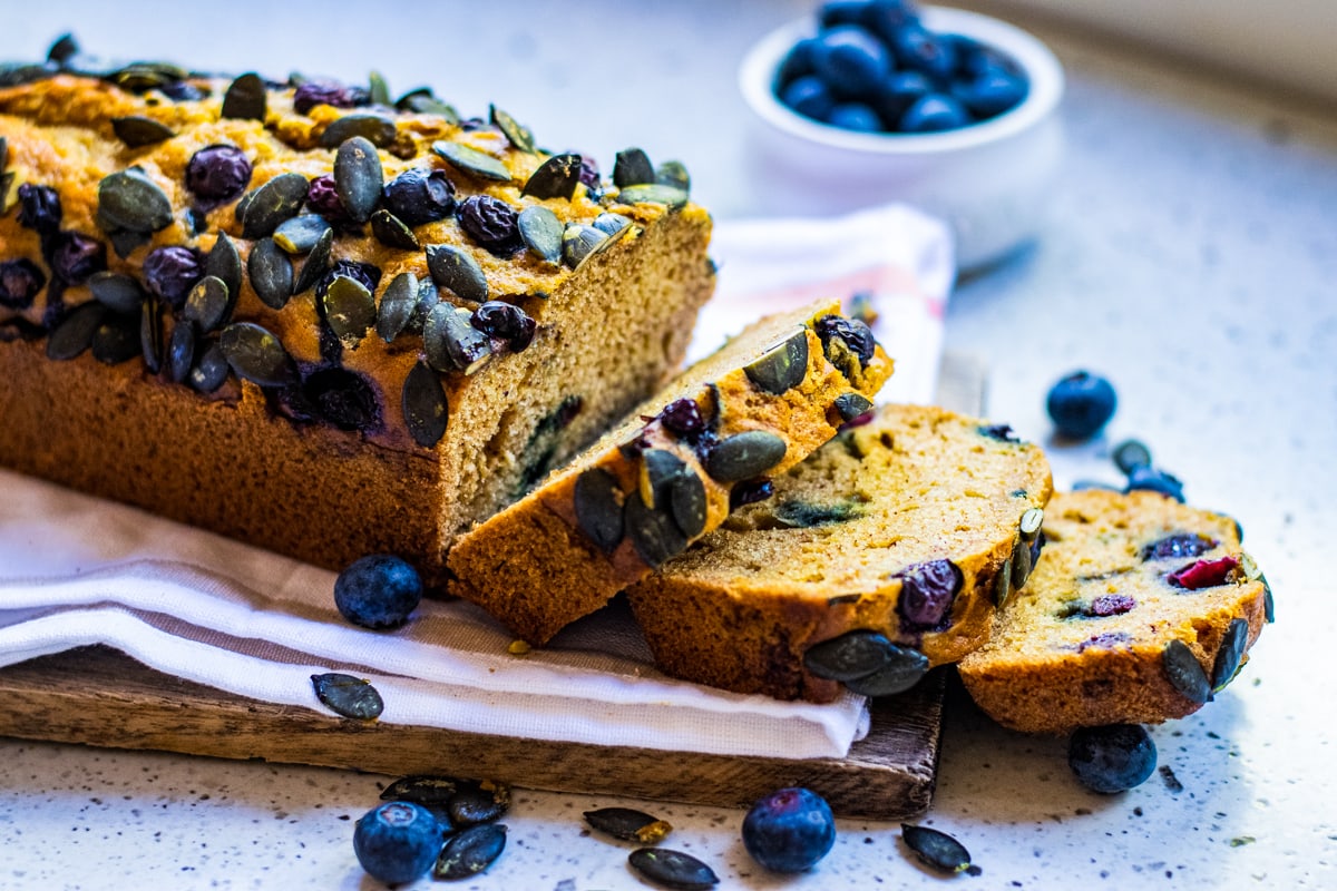 Blueberry pumpkin bread on a white towel with blueberries around.