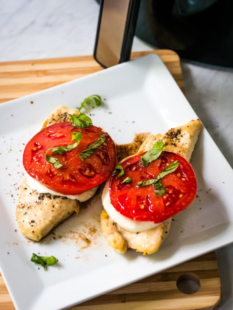 Chicken breasts with tomato and cheese in front of an air fryer
