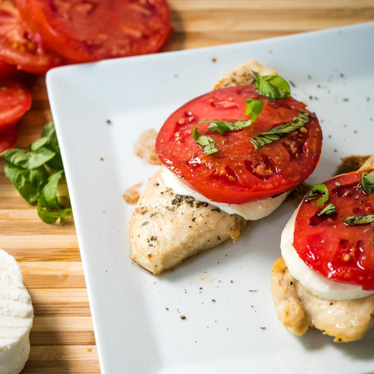 chicken caprese on a plate with tomatoes in the background