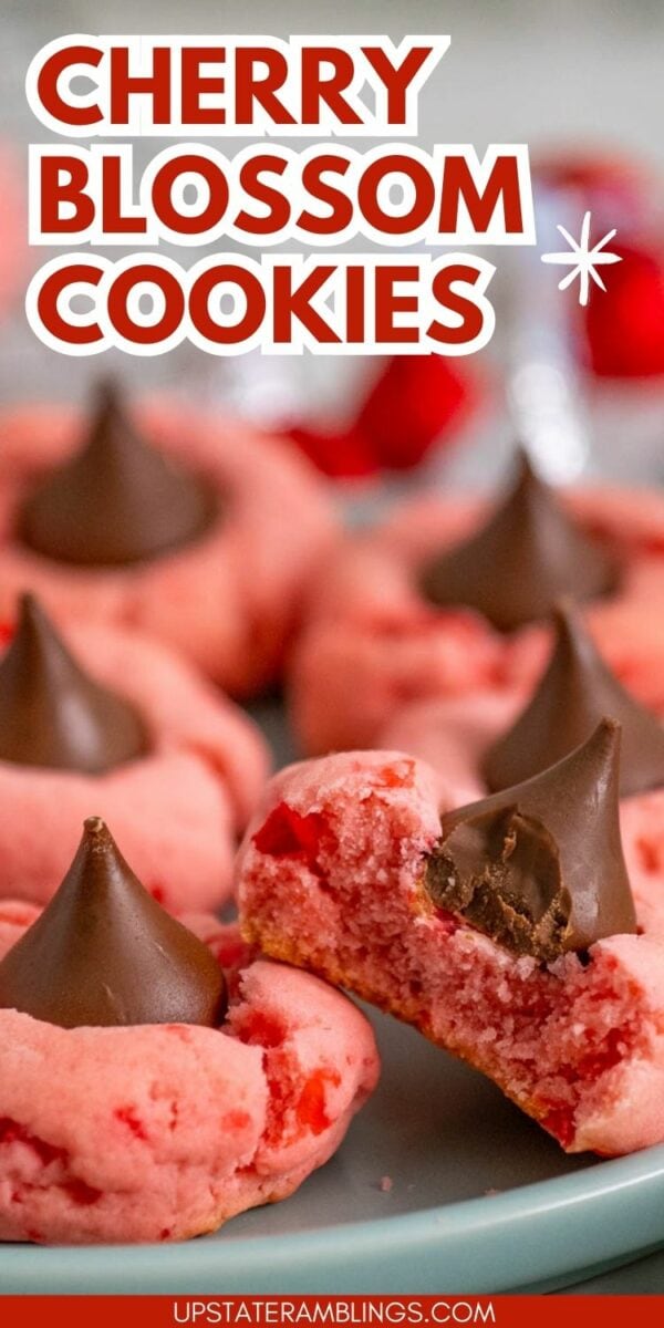 Close-up of cherry blossom cookies with pink dough and chocolate kisses on top. One cookie has a bite taken out, revealing the soft texture inside. The text "Chocolate Cherry Blossom Cookies" is at the top.