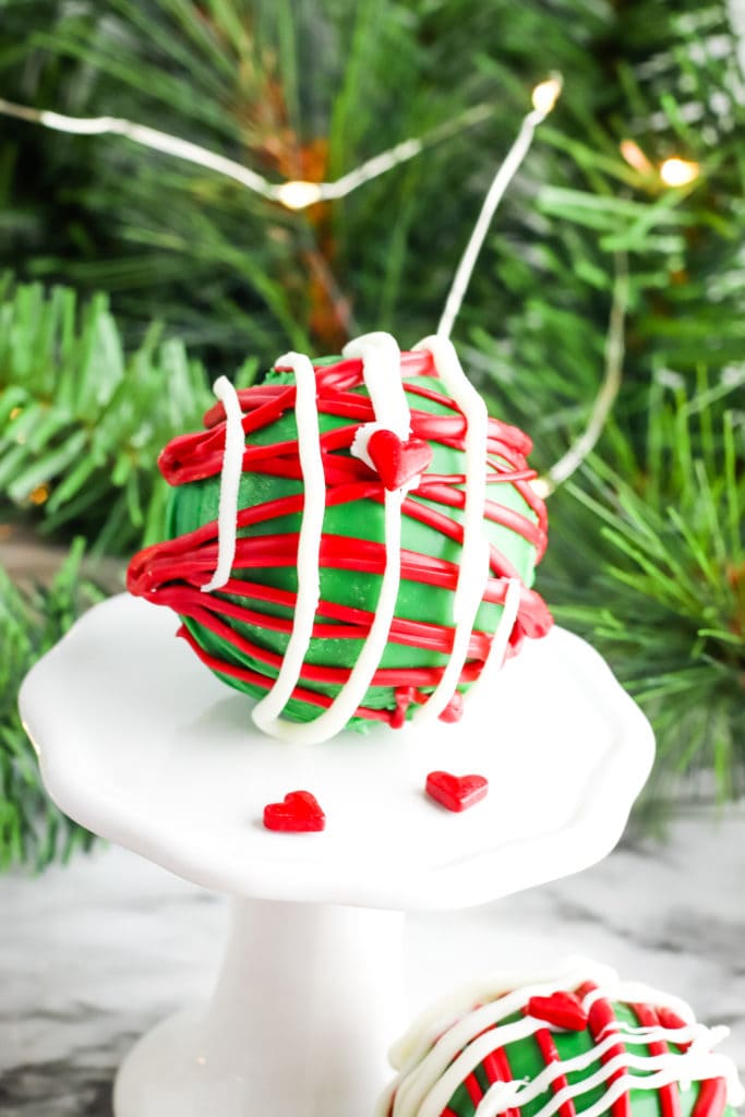 red and green Grinch hot chocolate bomb on a stand in front of an evergreen tree