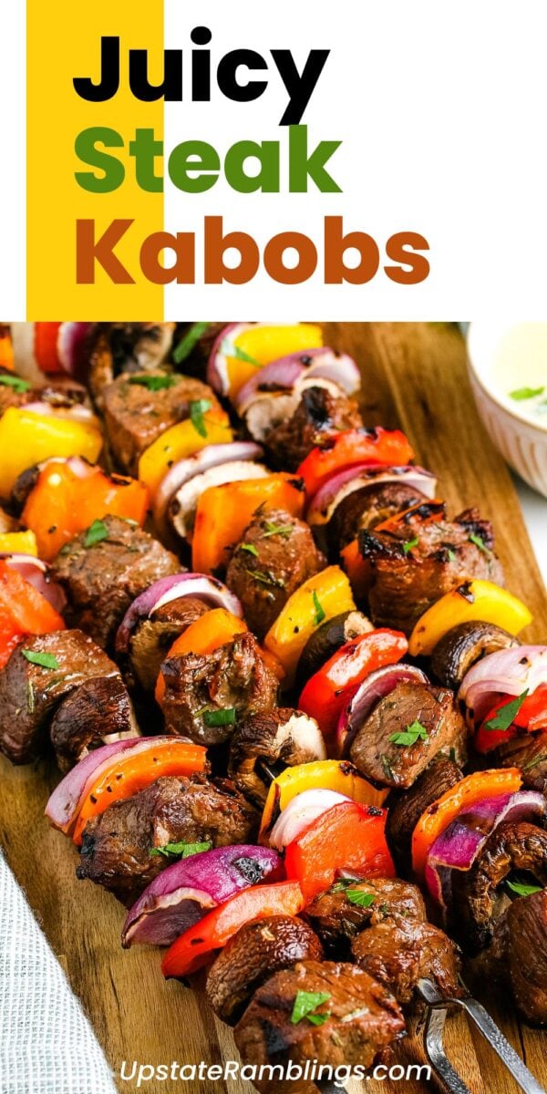 Grilled steak kabobs with red onions and colorful bell peppers are arranged on a wooden board, garnished with fresh herbs for a vibrant touch.