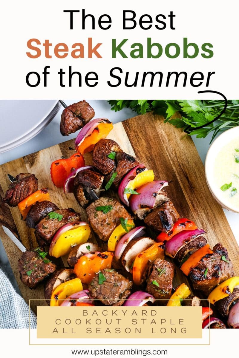 A platter of grilled steak kabobs with bell peppers and onions, garnished with herbs, sits beside a bowl of sauce and fresh parsley. Grilled steak kabobs are celebrated here as a summer cookout staple.