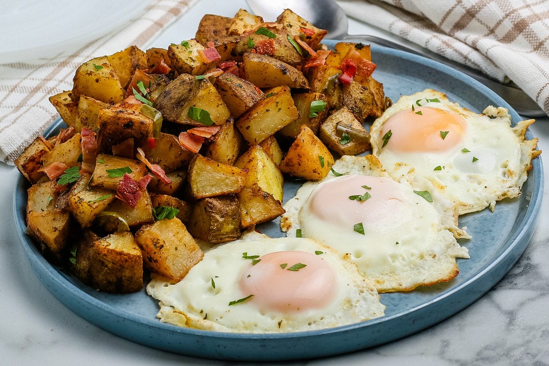 Breakfast potatoes on a plate with 3 eggs.