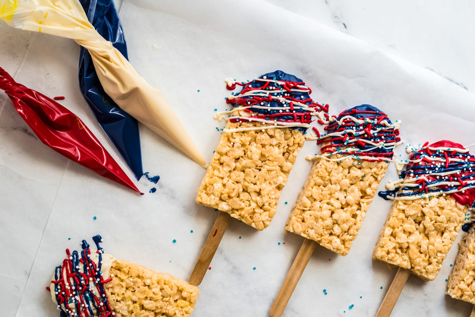 Rice krispie treats cut into popsicle shapes and drizzled with red, white and blue chocolate.