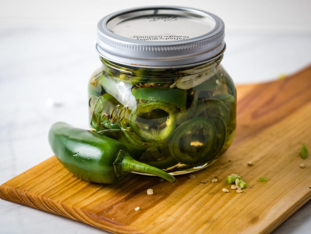 jar of pickles with jalapeno on a cutting board